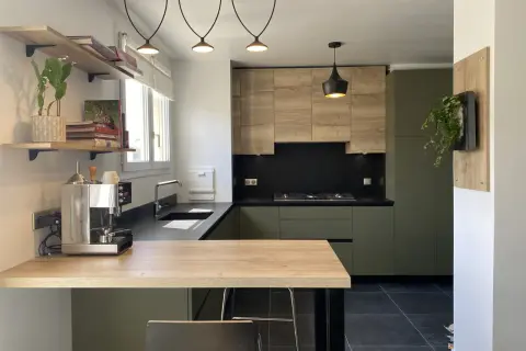Cuisine moderne avec meubles verts et bois, plan de travail noir et îlot en bois.