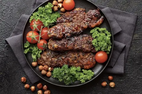 Saftiges Putenschnitzel braten, garniert mit Kirschtomaten, Petersilie und Haselnüssen auf schwarzem Teller.