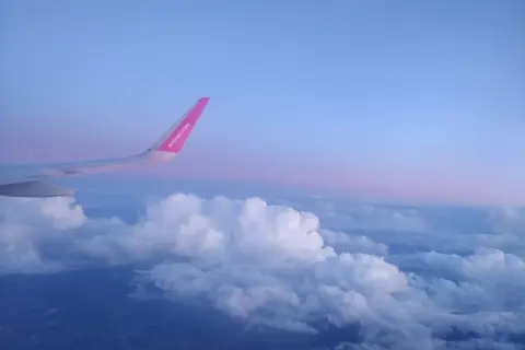 Skrzydło samolotu Wizz Air nad chmurami, wczesny poranek. Czas na loty do Anglii!