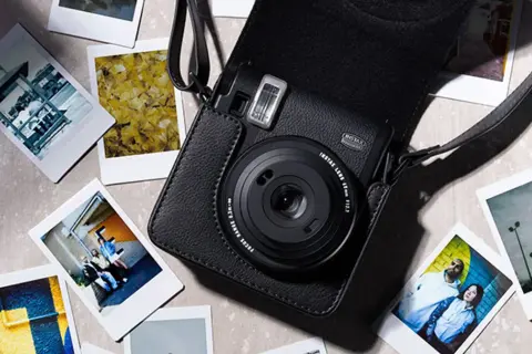 Czarny aparat Instax w futerale, otoczony natychmiastowymi zdjęciami. Dowiedz się, jak robić zdjęcia Instax, tworząc własne wspomnienia.