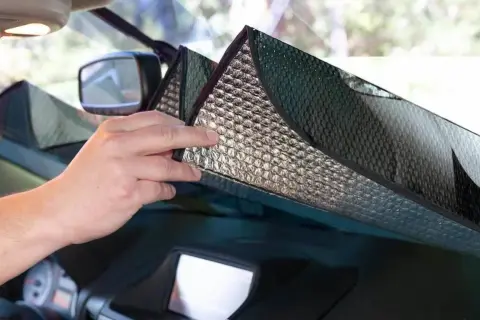 Mani che posizionano un parasole riflettente sul parabrezza per proteggere l'auto dal sole.