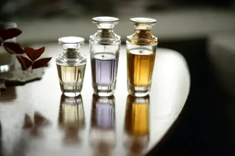 Trzy eleganckie flakoniki perfum o różnej zawartości i kolorze płynu, stojące na drewnianym stole.