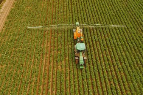 Traktor opryskuje pole roślin, stosując odpowiednią dawkę siarczanu magnezu ile na litr wody, by zapewnić im zdrowy wzrost.