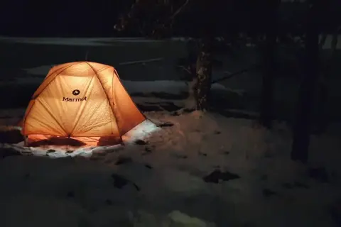 Upplyst tält i snön, redo för att sova ute på vintern.