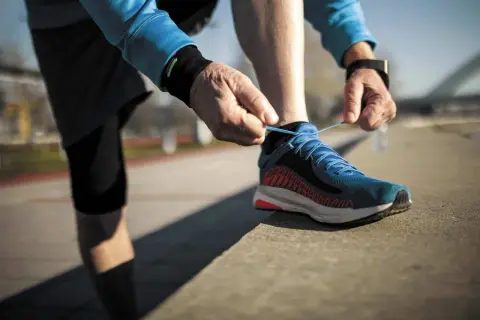 Un coureur attache ses lacets bleus, prêt à laisser une trace de frottement chaussure sur le bitume.