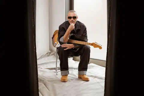 Alex Britti, con occhiali da sole e chitarra, sembra pensieroso, quasi gelido, mentre riflette sui suoi testi.