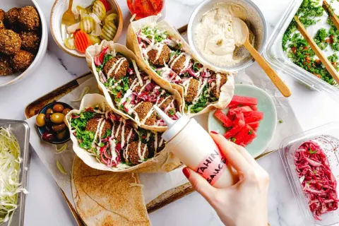 Leckeres Falafel-Rezept: Pita gefüllt mit Falafel, Salat, roten Zwiebeln und Tahini-Sauce. Dazu Hummus, Oliven und eingelegtes Gemüse.