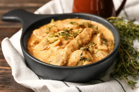 Cremiges Rindfleisch mit Pilzen, garniert mit frischem Thymian. Ein köstliches stroganoff rezept original, serviert in einer schwarzen Schüssel.