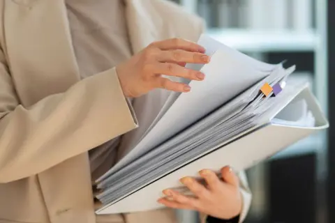 Dłonie przeglądają gruby segregator z dokumentami. To co to jest odpis dokumentu, który jest potrzebny do pracy.