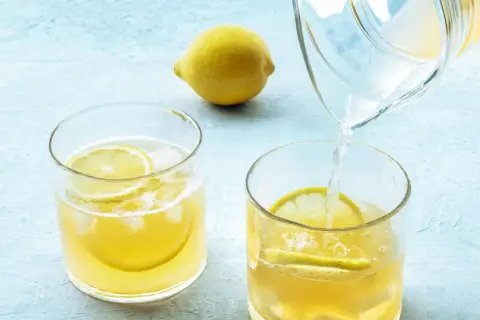 Erfrischendes Wasser mit Zitrone wird morgens in ein Glas mit Eis und Zitronenscheiben gegossen.