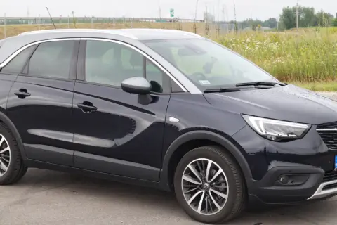 Ciemnogranatowy Opel Crossland z dwukolorowym dachem, stojący na tle łąki. Wady i zalety tego modelu to temat dyskusji.