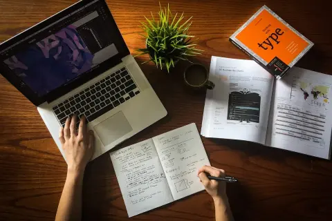 Ręce pracują nad projektem, laptop, notatnik i książka o typografii. To idealne warunki do start up.