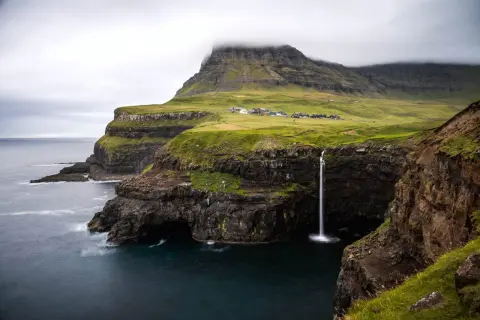 Paysage spectaculaire des îles Féroé : une cascade tombe d'une falaise verdoyante dans l'océan. Idéal pour une randonnée inoubliable.