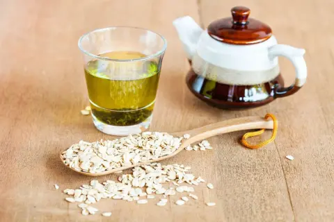 Verre de thé vert, théière et cuillère en bois remplie de flocons d'avoine. Découvrez les mugicha bienfaits pour une boisson rafraîchissante.