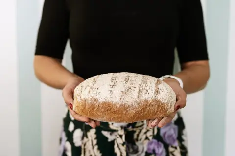 Kobieta trzyma bochenek chleba razowego. Zastanawiasz się, ile kcal ma kromka chleba razowego? Ten pyszny chleb może być częścią zdrowej diety.