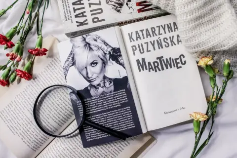 Książki Katarzyny Puzyńskiej, kwiaty i szkło powiększające na białym tle.