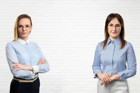 Dwie kobiety w koszulach na tle białej ceglanej ściany.
