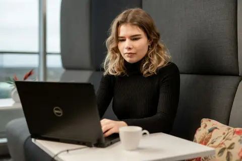 Młoda kobieta z wrodzonymi zdolnościami do pracy przy laptopie, skupiona na zadaniu. Obok filiżanka kawy.