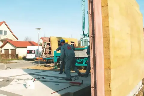 Budowa domu z keramzytu. Pracownicy montują prefabrykowaną ścianę na placu budowy.