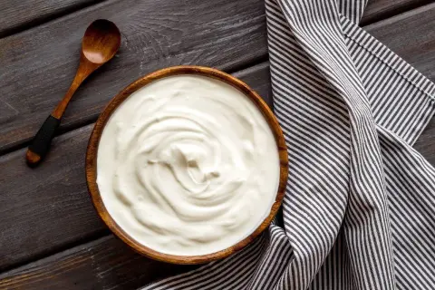 Prosty krem z mascarpone i jogurtu w drewnianej misce, obok drewniana łyżka i pasiasty ręcznik.