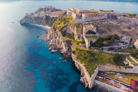 Fortificazioni storiche su una costa rocciosa con mare blu intenso. Un'idea per cosa visitare in Toscana in 2 giorni, tra storia e natura.