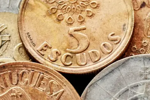 Złote monety z napisem "ESCUDOS" i cyfrą 5, dawna waluta Portugalii przed euro.