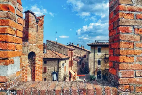 Un antico borgo vicino Parma, con case in pietra e tetti rossi, incorniciato da mura di mattoni sotto un cielo azzurro e nuvoloso.