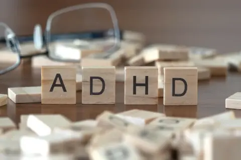 Drewniane klocki z literami "ADHD" i rozrzucone po stole, sugerujące poszukiwanie rozwiązań, np. leki na ADHD.