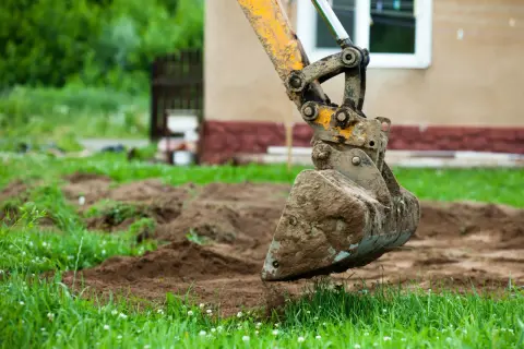 Koparka z brudną łyżką pracuje na nierównym terenie. Może to oznaczać kary za niwelację terenu.