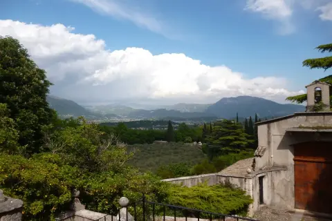 Panoramica sul percorso eremo dei camaldolesi Bardolino, con vista su colline, uliveti e montagne sotto un cielo nuvoloso.