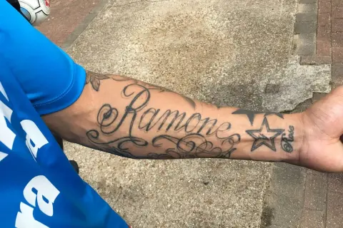 Damski tatuaż na przedramieniu z napisem "Ramone" i gwiazdką.