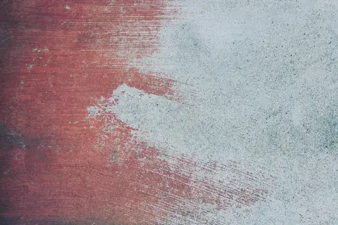 Texturen av ett betonggolv utomhus, delvis målat med röd färg. Penseldragen syns tydligt.