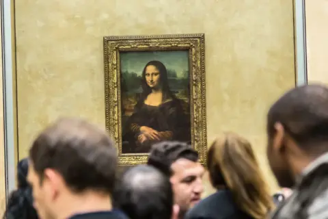 Mona Lisa z Isleworth, otoczona tłumem widzów, spogląda tajemniczo ze złotej ramy.