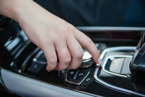 Main d'une personne actionnant un bouton sur la console centrale d'une voiture, peut-être pour savoir comment débloquer un frein à main automatique.