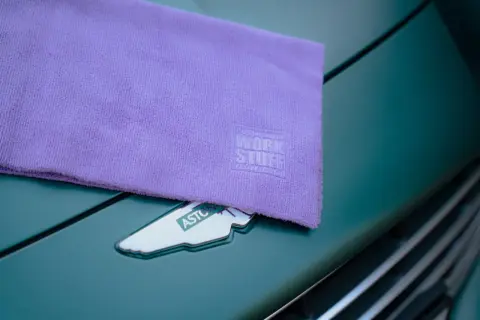 Fioletowa mikrofibra z logo Work Stuff na masce Aston Martina. Idealna do pielęgnacji auta.