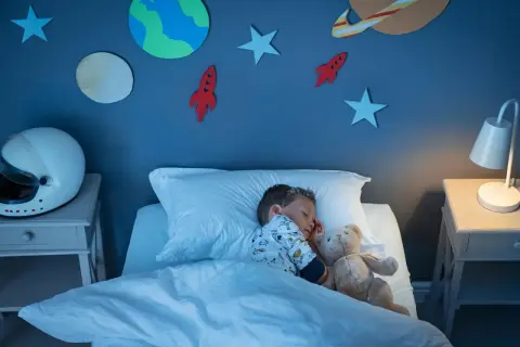Kleiner Junge schläft im Weltraum-Kinderzimmer. Die kinderzimmer wandgestaltung mit Planeten und Raketen inspiriert Träume von Abenteuern.
