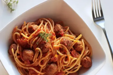 Pyszne spaghetti z klopsikami w sosie pomidorowym, udekorowane gałązką tymianku. Idealne pytanie: jakie przyprawy do spaghetti?