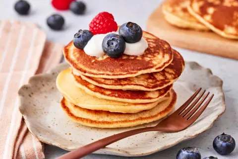 Ein Stapel goldbrauner Pancakes mit Joghurt, Blaubeeren und einer Himbeere obendrauf. Ein köstlicher pancake mit joghurt für ein perfektes Frühstück.
