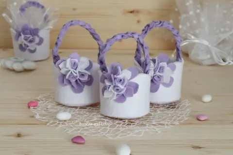 Piccoli cestini porta bomboniere fai da te in feltro bianco con fiori lilla e manici intrecciati, perfetti per un evento speciale.