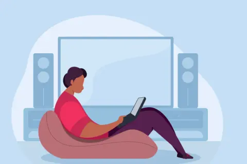 Person im Sessel mit Laptop, vor einem großen Bildschirm und Lautsprechern. Ein Beispiel für hybrides Arbeiten, flexibel und bequem.