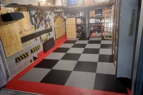 Pavimento a scacchi in piastrelle carrabili per garage, con bordi rossi e pareti attrezzate per gli attrezzi.