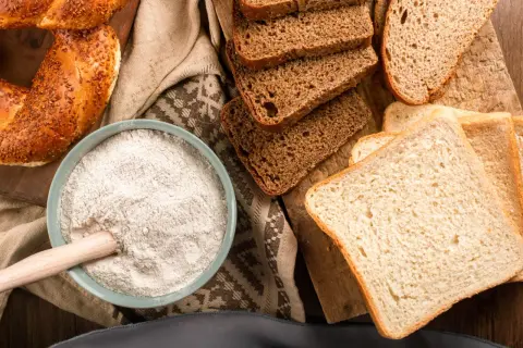 Mąka w misce, kromki chleba i bułka. Czy mąka kukurydziana ma gluten? To pytanie nurtuje wielu piekarzy.