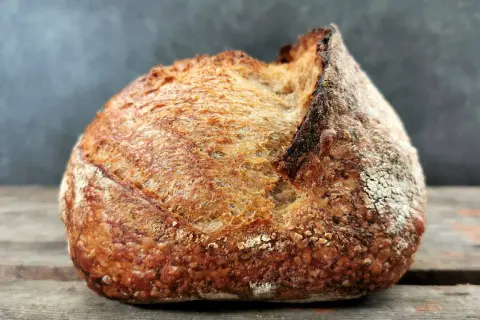 Ein rustikales Brot mit knuspriger Kruste und luftiger brot krume liegt auf Holzbrettern.