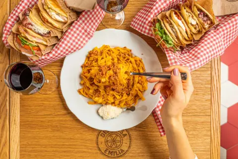Tagliatelle al ragù, un classico italiano. Accanto, piadine farcite e un bicchiere di vino rosso.