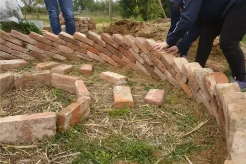 Costruzione di un keyhole garden con mattoni. Mani che posizionano i mattoni per creare la forma circolare.