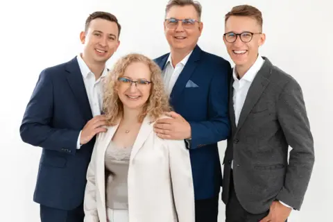 Cztery osoby w eleganckich strojach, uśmiechnięte, na białym tle.