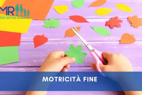 Mano di bambino che ritaglia forme di foglie colorate con forbici rosa, un'attività che stimola la motricità fine.