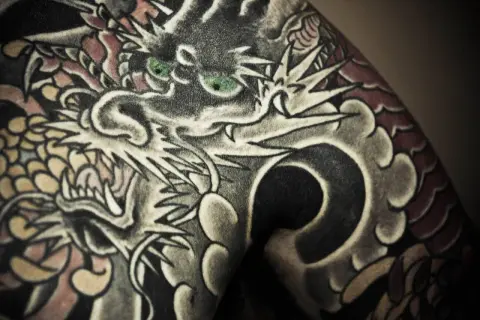 Ein detailreiches Irezumi Tattoo zeigt einen Drachenkopf mit grünen Augen, der sich über die Haut schlängelt.