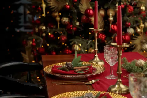 Une élégante deco table noel rouge et or, avec des bougies, des ornements dorés et un sapin scintillant en arrière-plan.