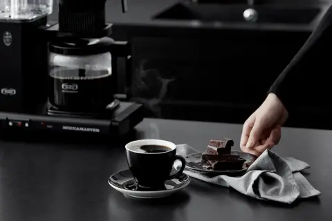 En kopp ångande kaffe från Moccamaster, perfekt för en stunds njutning. Visste du att kaffe nyttigt kan vara? Mörk choklad bredvid.